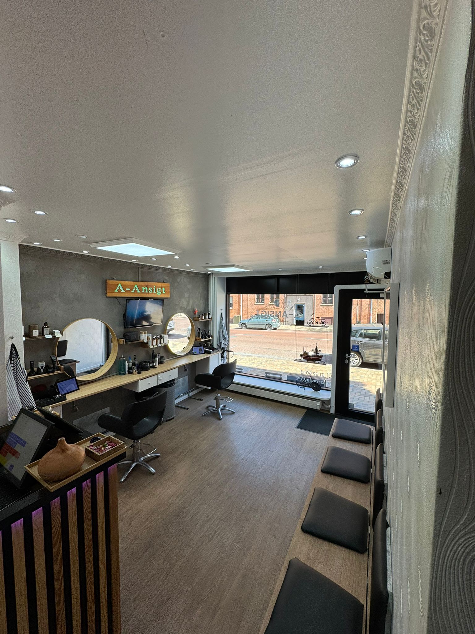 Kig fra arbejdspladsen mod indgangen — bænk med sorte hynder og dagslys fra gaden