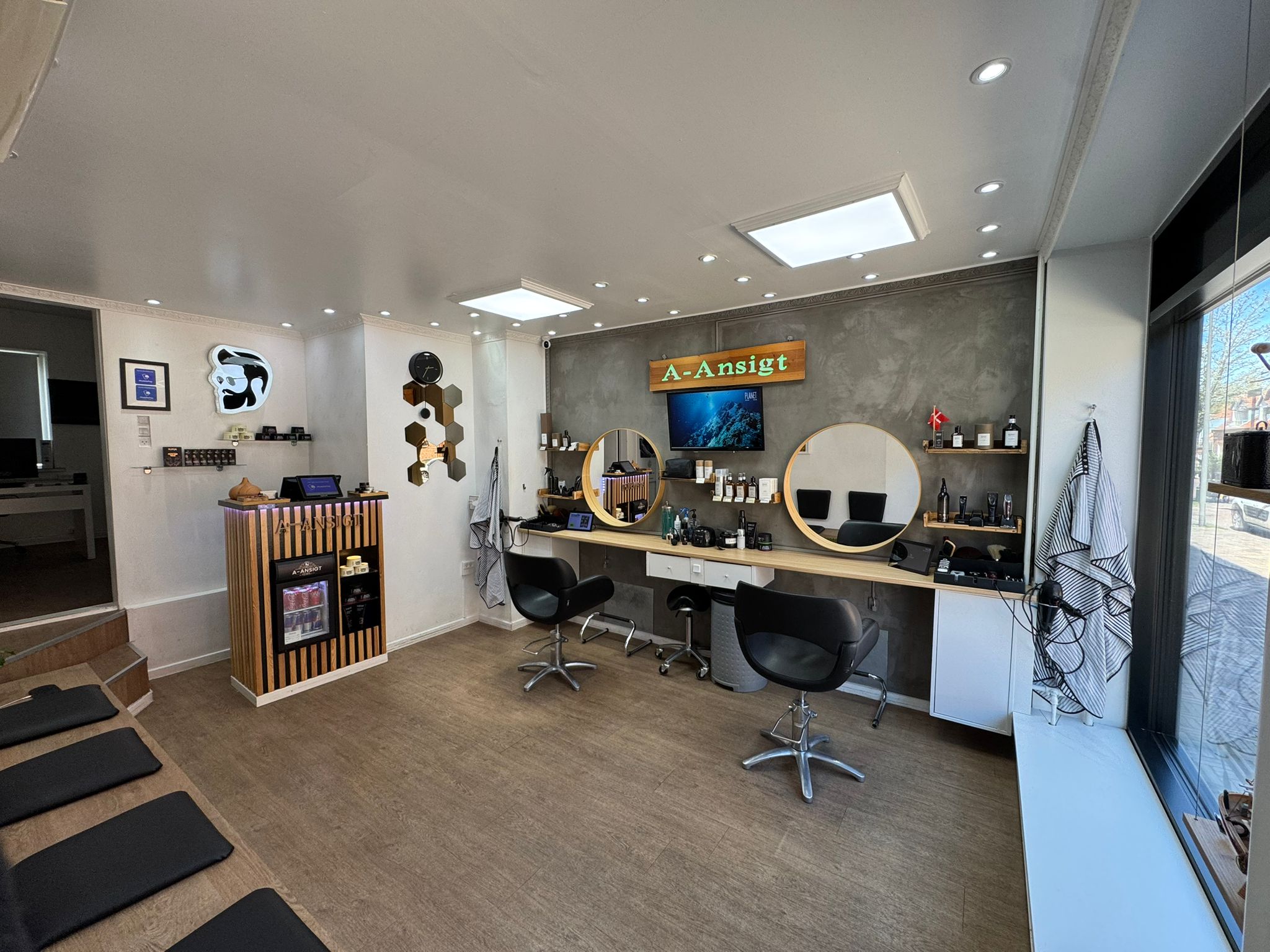 Salonen indefra — to klippestole, runde spejle og A-Ansigt skiltet over arbejdspladsen